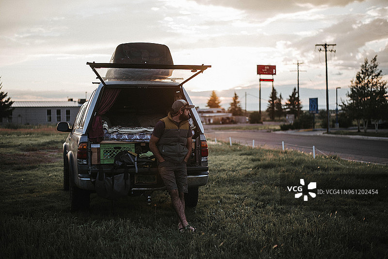 日落时分，男子站在草地上车辆旁，背景是天空图片素材