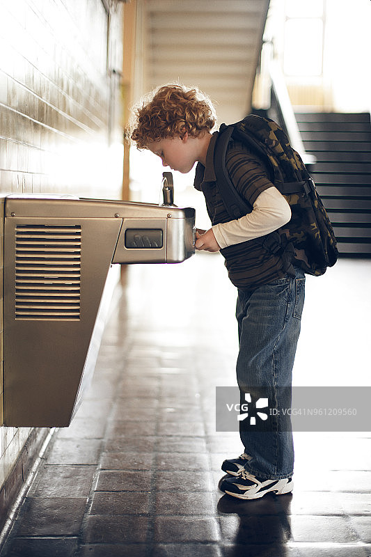 男孩在学校饮水台喝水的侧面照图片素材