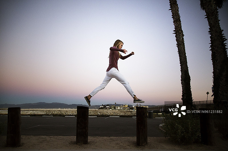侧视角度拍摄的女子，在城市中跳跃于木桩之上图片素材