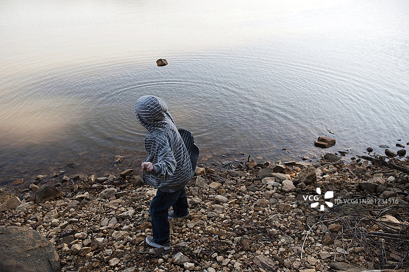 男孩穿着帽衫在湖中扔石头的侧面照图片素材