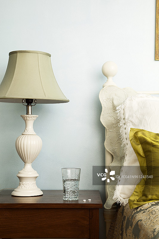 卧室床头柜上，台灯旁放着药丸和玻璃杯图片素材