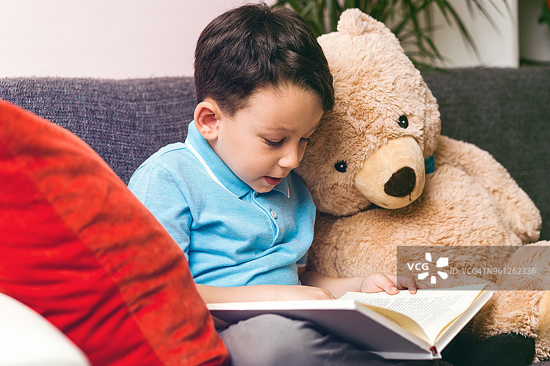 小男孩给泰迪熊朋友读书图片素材