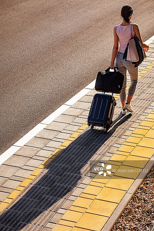 一位年轻女子在人行道上行走，拉着一个带轮子的小行李箱的后视俯视照片图片素材