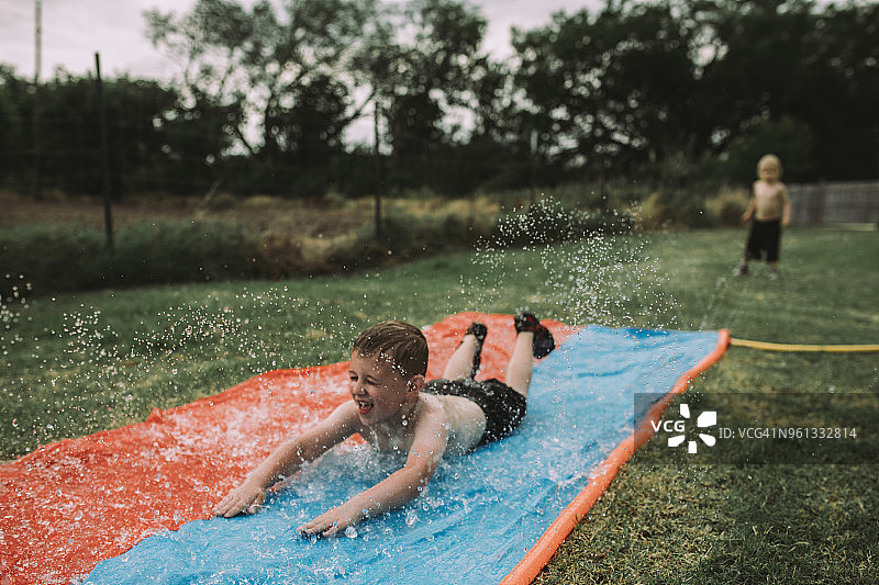 在院子里滑滑梯，哥哥站在背景中的男孩图片素材