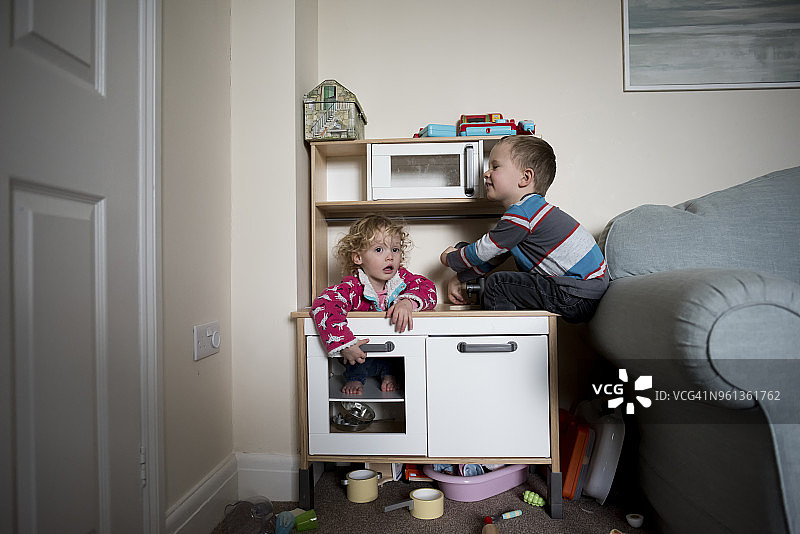 兄妹在家里的沙发旁边的柜子上玩耍图片素材