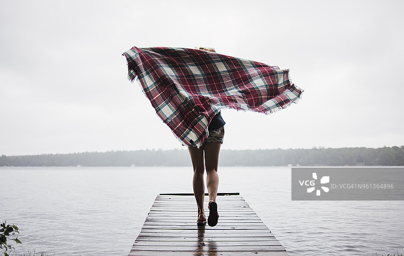 无忧无虑的女人在Kawartha湖上，拿着毯子在码头上奔跑的背影图片素材