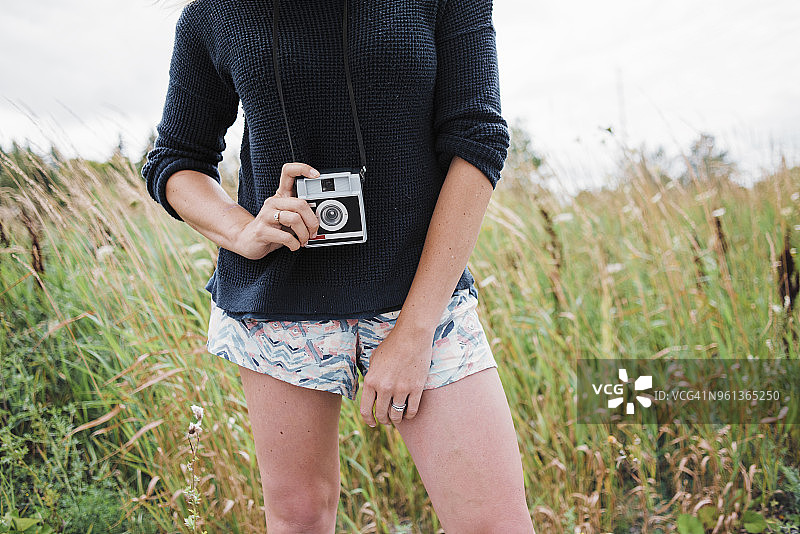 女子站在草地上手持拍立得相机的腰部特写图片素材