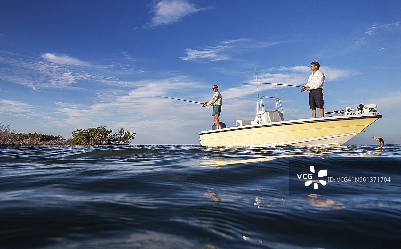 低角度拍摄：男人们站在船上对着天空钓鱼图片素材