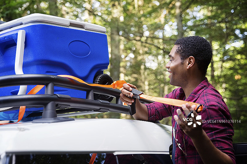 度假时，快乐的男人将冰桶绑在汽车顶架上图片素材