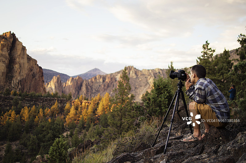 徒步旅行者在秋季坐在山上拍照的侧视图图片素材