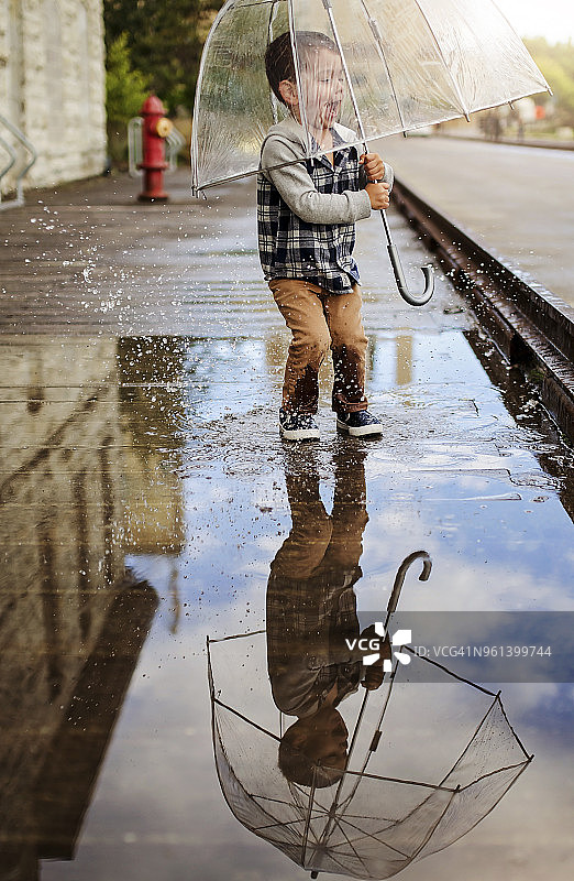 在街上拿着雨伞在水坑上跳跃的顽皮男孩图片素材