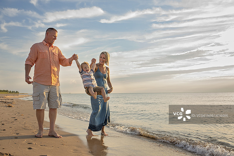 快乐的父母在海滩上牵着儿子的手荡秋千图片素材