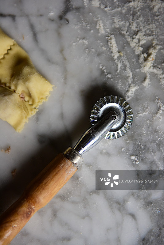 厨房大理石台面上带有面粉和新鲜制作的 tortellini 的意大利面切割轮图片素材