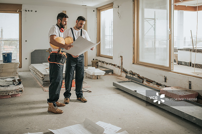 建筑工人在公寓里分析蓝图的全身照图片素材