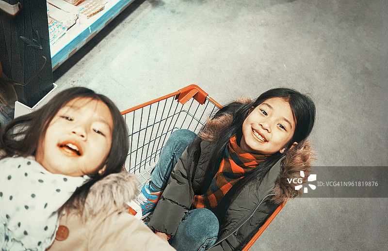 两个女孩坐在超市的购物车里图片素材
