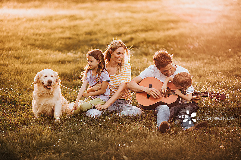 春天，幸福的年轻家庭和他们的狗在公园草地上放松身心。图片素材