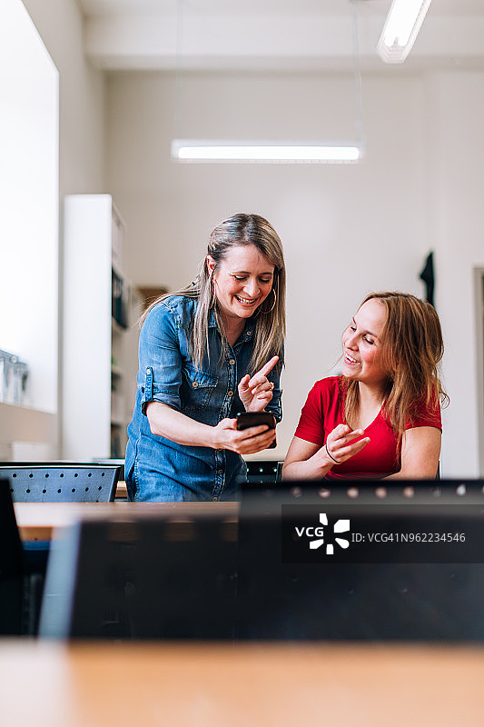 老师和成年学生看手机并笑着图片素材