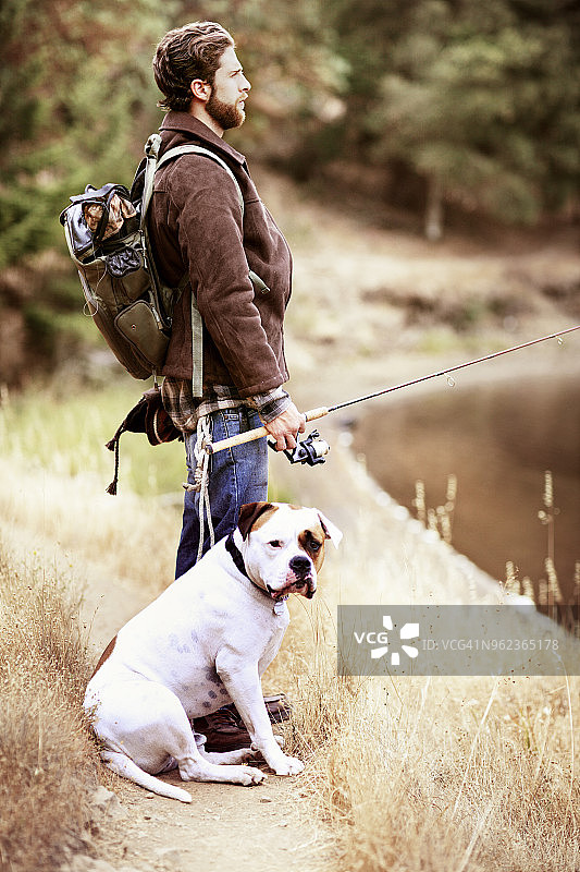 旅行者与爱犬在湖岸边垂钓图片素材