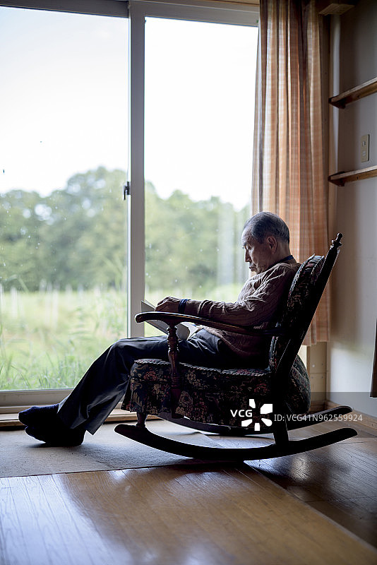 坐在窗边摇椅上读书的老年男人图片素材