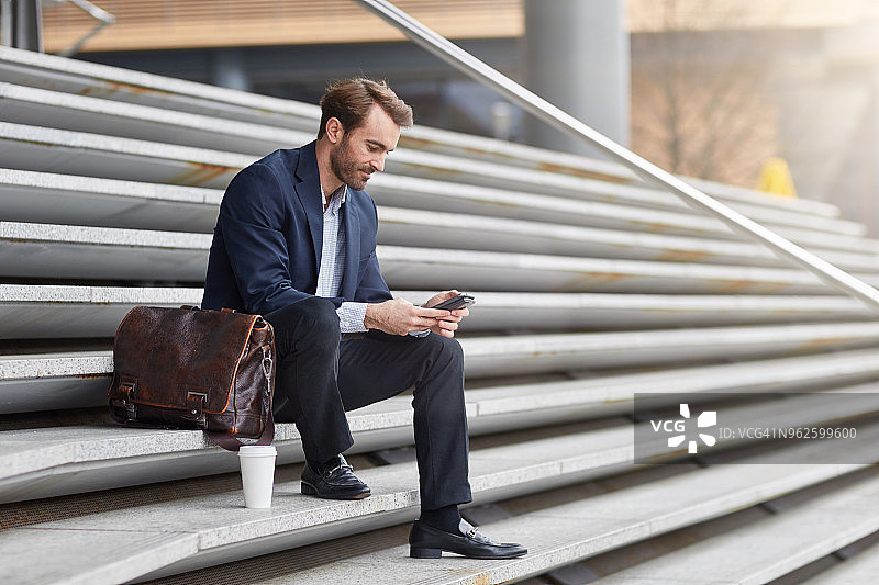 坐在户外台阶上用手机发短信的商人图片素材