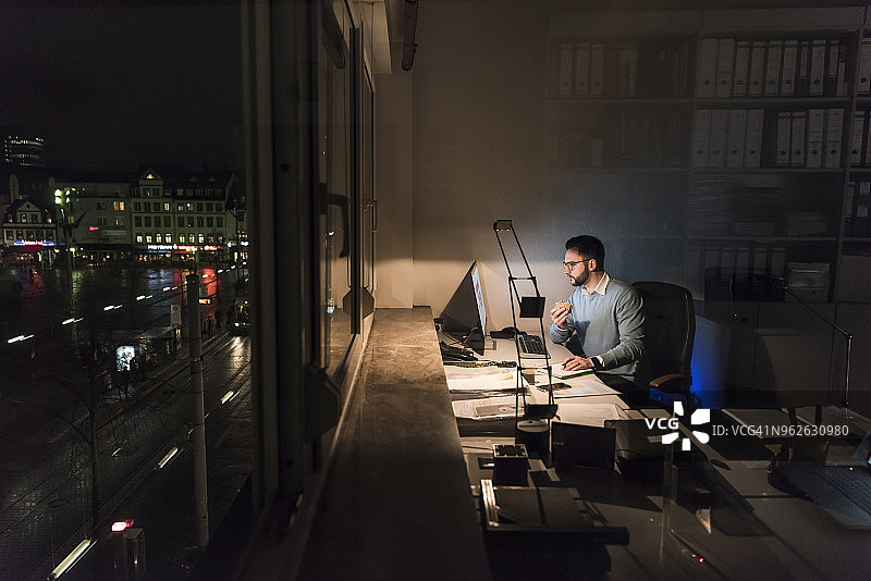 商务男士在夜晚的办公室里使用电脑工作图片素材