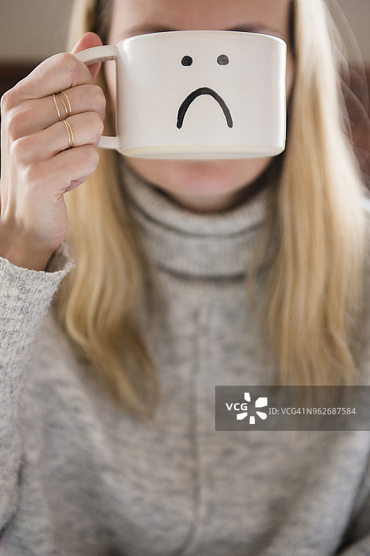手持悲伤表情马克杯挡住脸的女人图片素材
