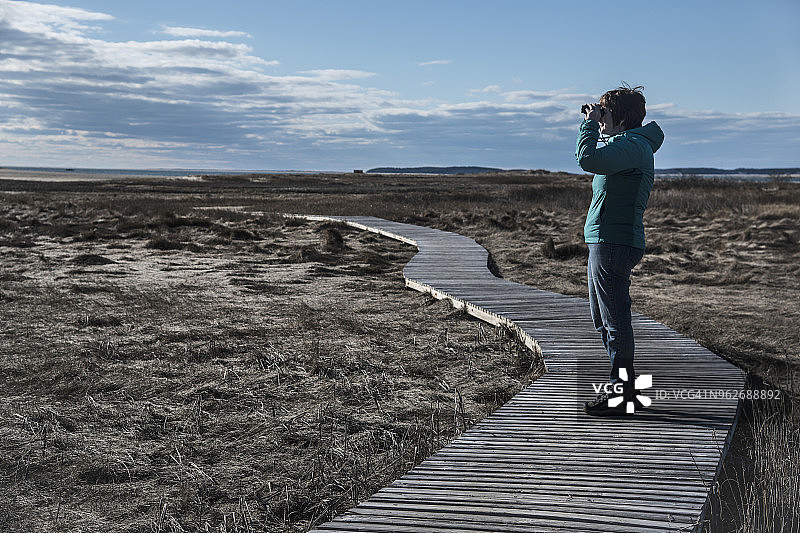 美国马萨诸塞州科德角韦尔弗利特站在木板路上手持望远镜的女人图片素材