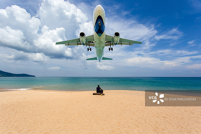 年轻男人坐在迈考海滩上，背景是飞机图片素材