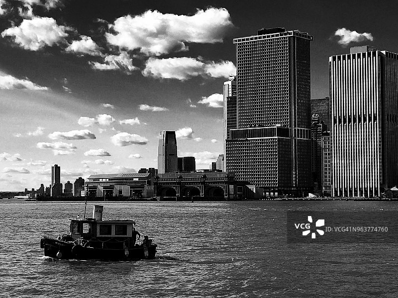 曼哈顿下城天际线和东河的黑白景观，前景是布鲁克林河岸拍摄的纽约港拖船，戏剧性的云景天空图片素材