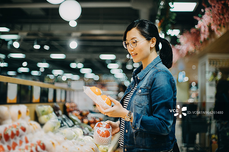 年轻亚洲女性在超市购买新鲜有机水果图片素材