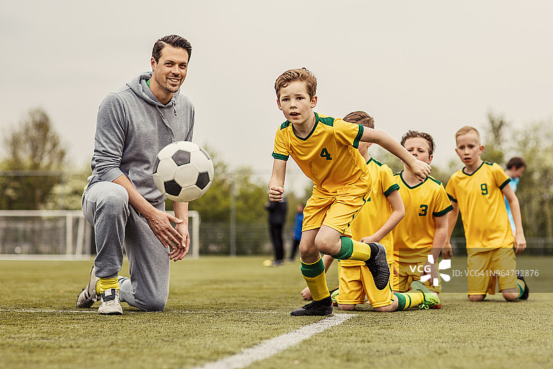一位英俊的男教练带领男孩足球队进行紧张的足球训练图片素材