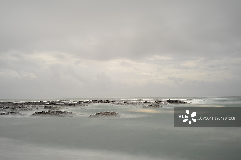多云天空下，海中岩石的田园风光图片素材