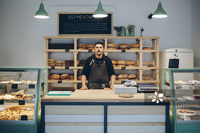 自信的面包师站在面包店柜台前的肖像图片素材