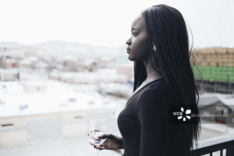 酒店阳台上，若有所思的女商人拿着饮料，看向远方的侧面景观图片素材