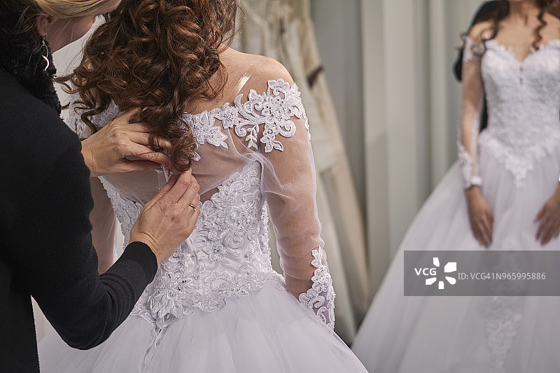设计师在商店协助新娘试穿婚纱的侧视图图片素材