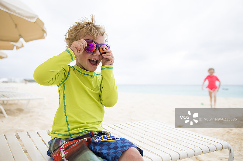 在沙滩躺椅上戴着闪亮太阳镜的顽皮男孩图片素材