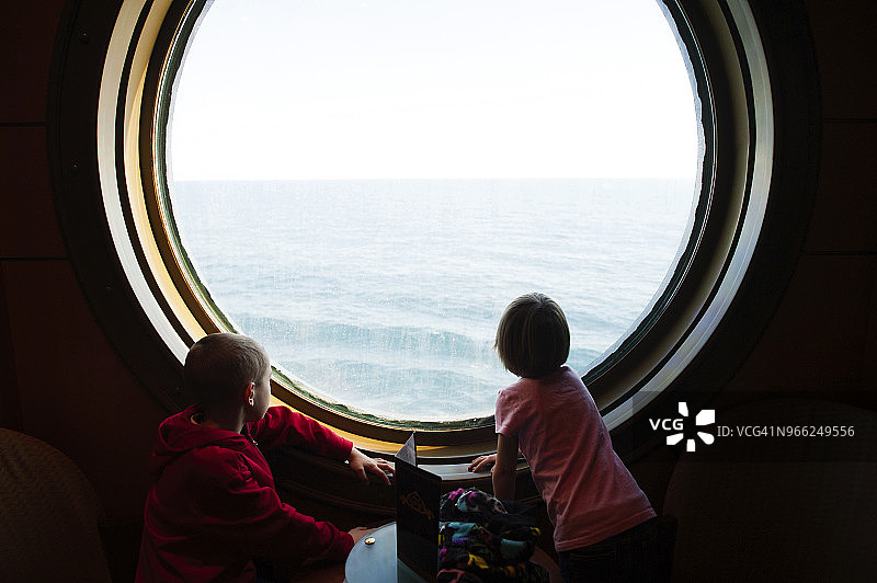 兄妹或姐弟站在游轮舷窗旁看海图片素材
