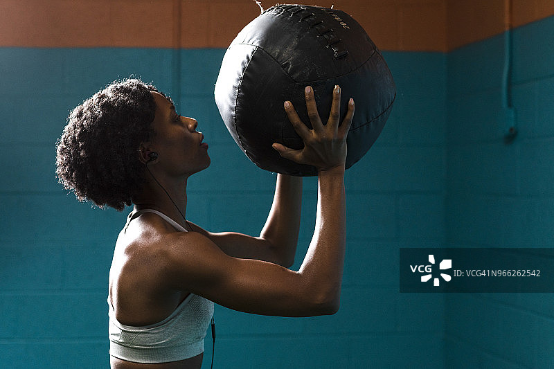 女人在健身房靠墙听音乐，手持健身球的侧视图图片素材