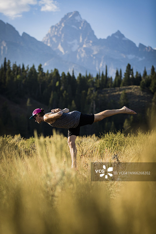 男人在布里杰-蒂顿国家森林公园的田野上单腿练习瑜伽的侧面视角图片素材