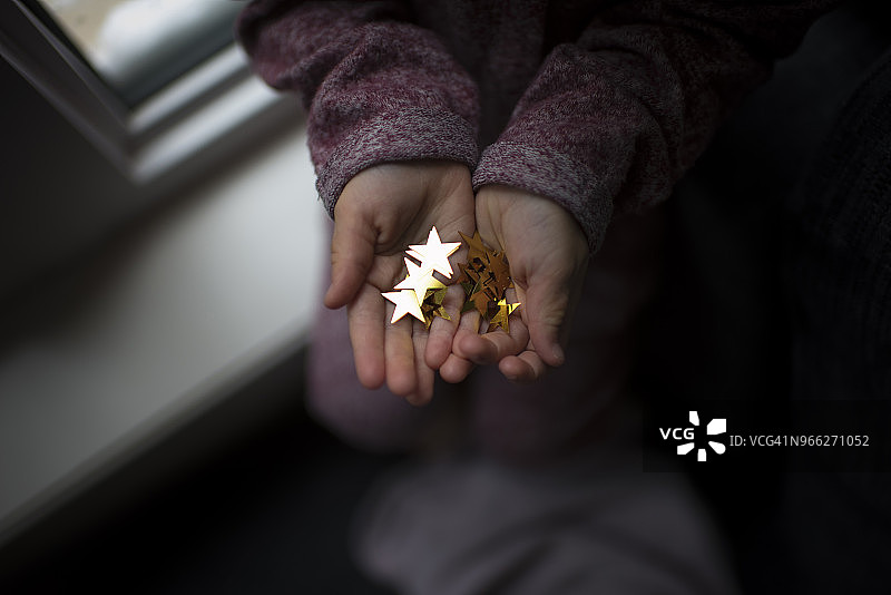 坐在暗房窗台上拿着星形装饰品的女孩的裁剪图图片素材