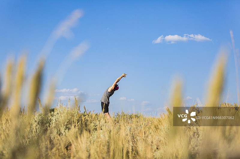 在布里杰-蒂顿国家森林，男子在田野上对着天空练习瑜伽伸展手臂图片素材