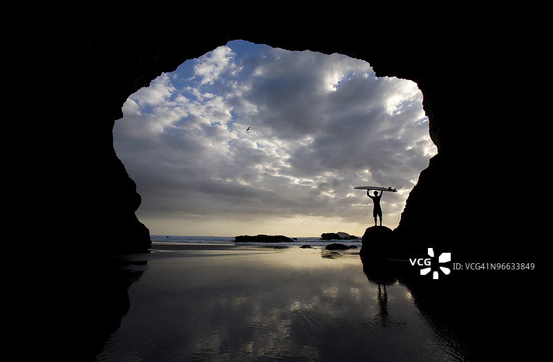 新西兰北岛穆里怀海滩洞穴中的冲浪者剪影图片素材