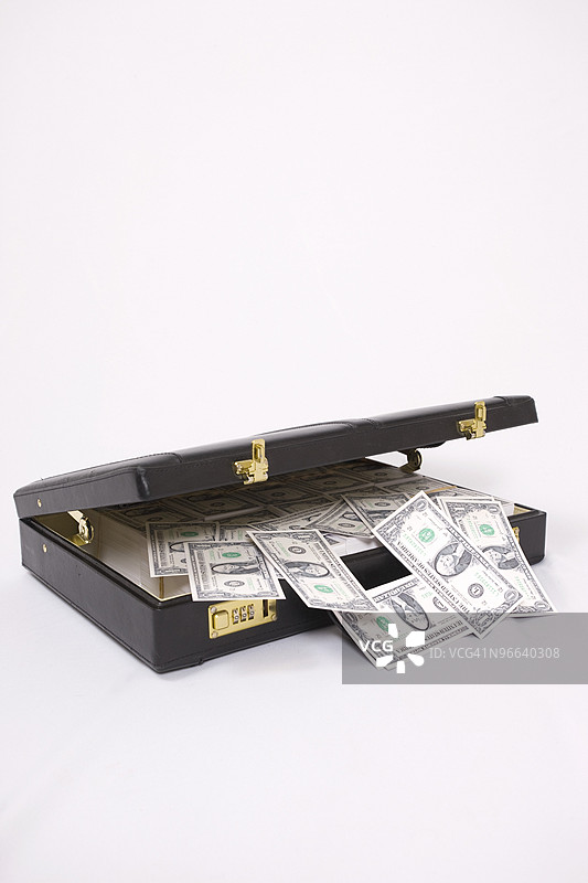 装满现金的公文包倾斜着，钱币洒落出来图片素材