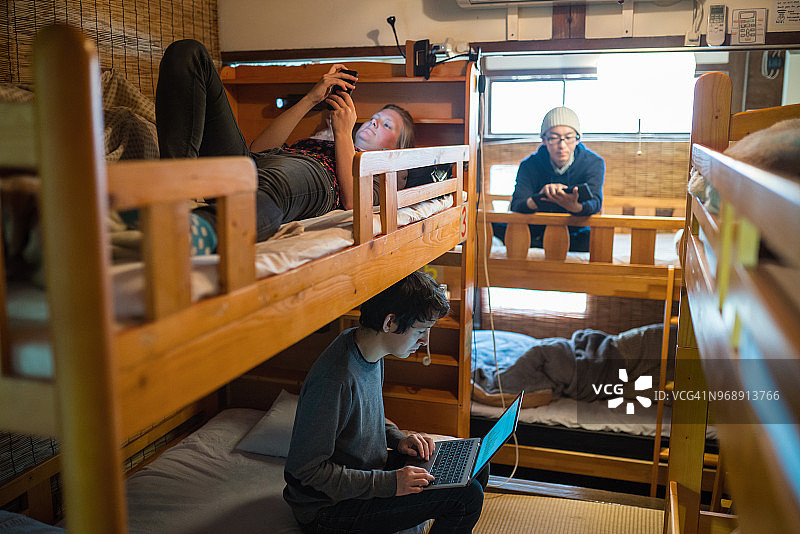 在宿舍式背包客旅馆中使用笔记本电脑的年轻旅行者图片素材