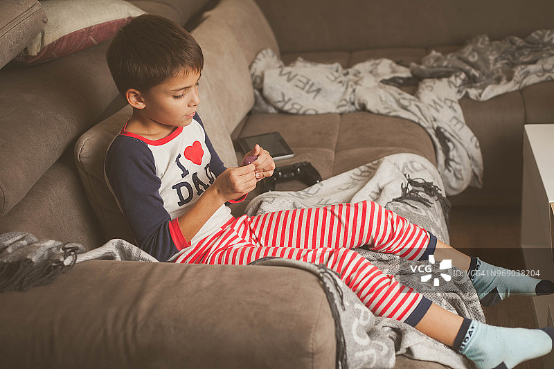 穿着睡衣的可爱白人男孩坐在凌乱的沙发上玩泥图片素材