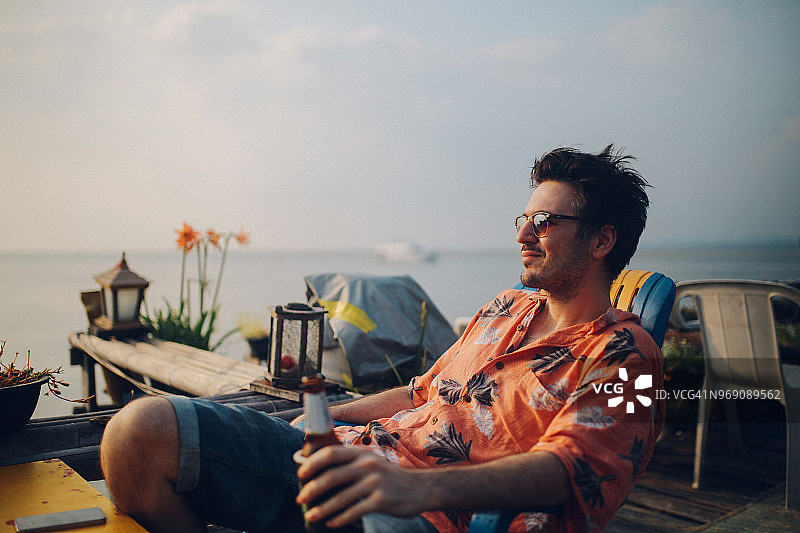 年轻男人在泰国兰塔岛海边喝啤酒看日落图片素材