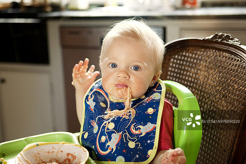 在家中坐在高脚椅上吃面的男婴肖像图片素材