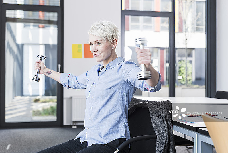 在办公室用哑铃锻炼的微笑女人图片素材