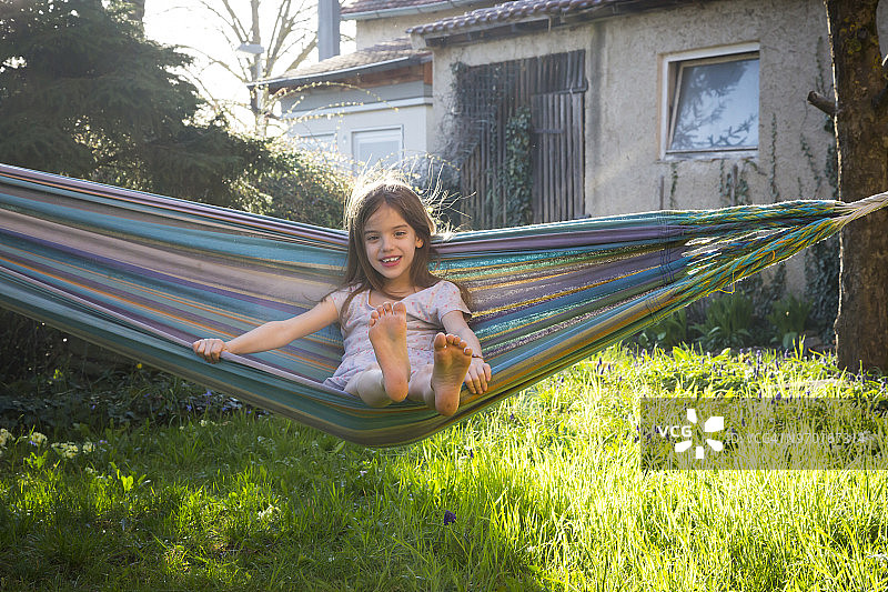 微笑小女孩坐在花园吊床上的肖像图片素材