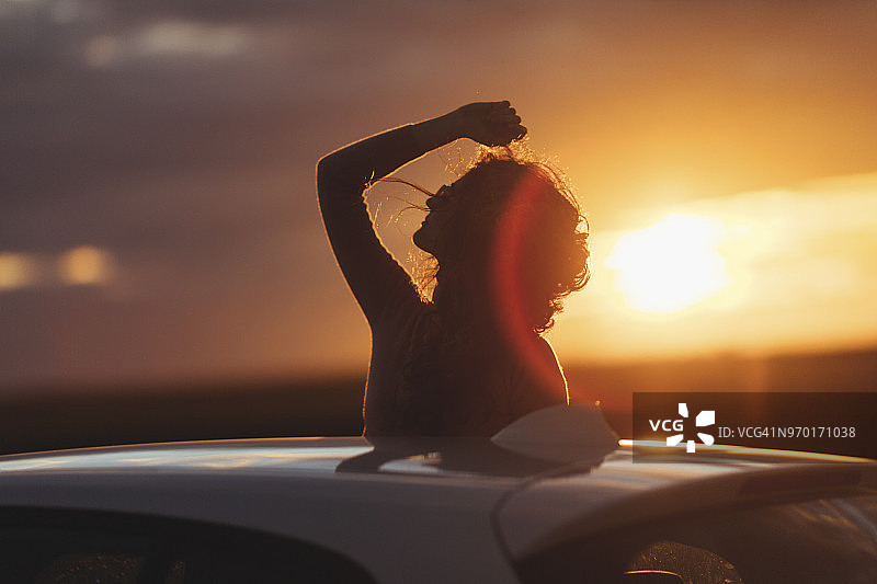 日落时在车外举起手臂的女人图片素材